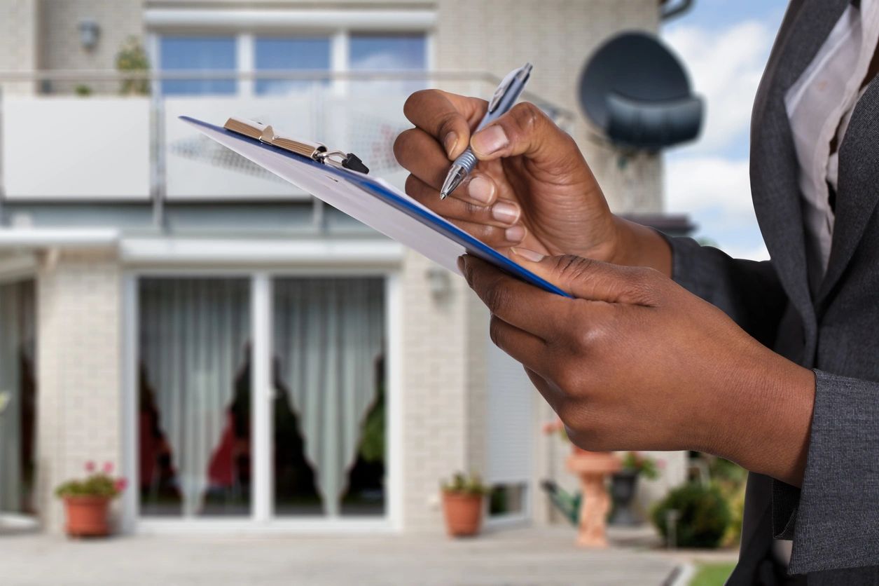 A person holding a pen and paper in front of a house.